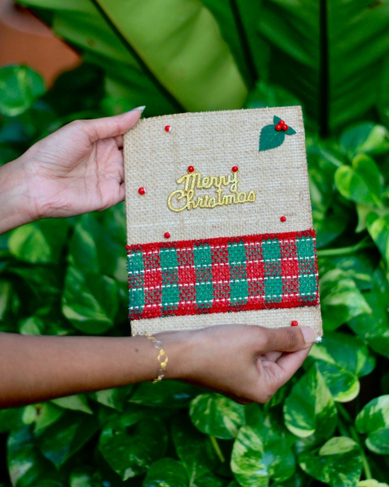 Hands holding a handmade jute Christmas wish card with a tartan ribbon