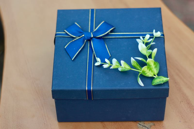 Navy gift box tied with a satin bow and a sprig of greenery